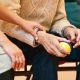 Altenpflegerin hält die Hand einer älteren Person in einem Sitzkreis, ältere Person hat einen kleinen Spielball in den Händen